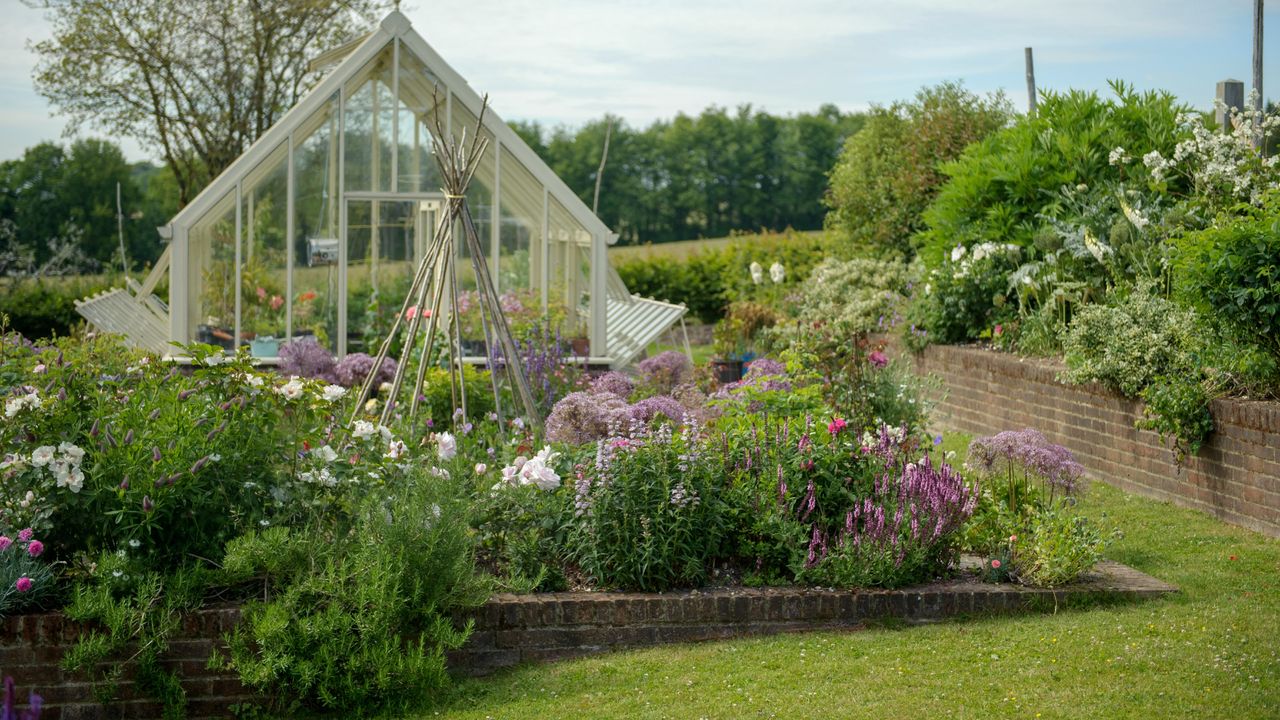 A blooming garden with borders and a greenhouse