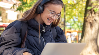 A student wearing headphones using a laptop outdoors