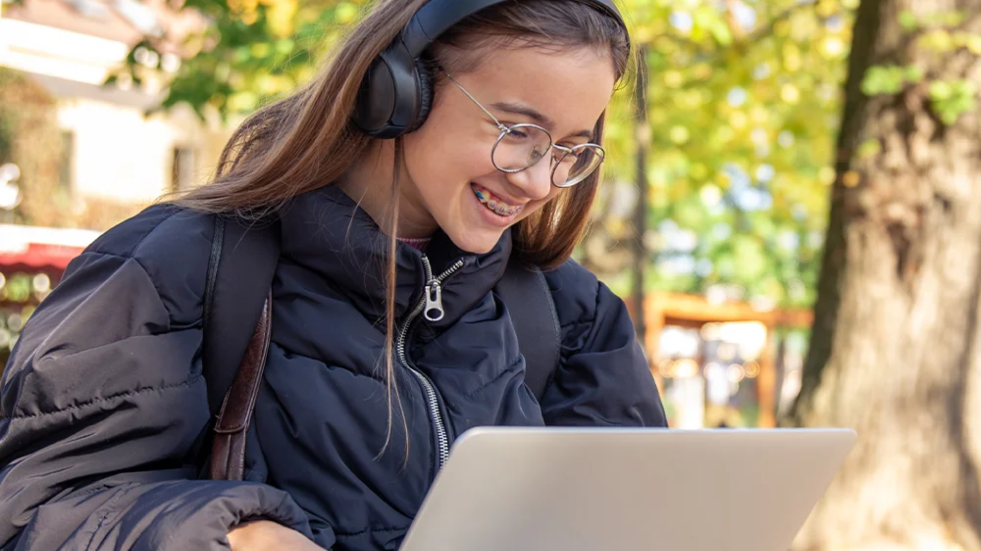 A student wearing headphones using a laptop outdoors