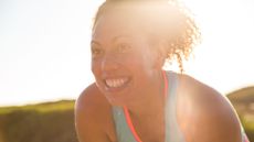 Woman leaning towards the camera smiling wearing workout clothes, representing causes behind why does my face sweat so much