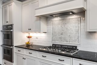 A white kitchen with white tiles and black countertops, with under cabinet lighting.
