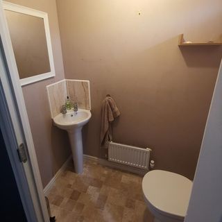 Small bathroom with light brown walls, brown square tiles, toilet and sink.