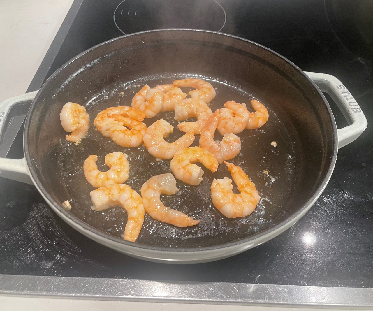 Frying shrimp inside a shallow fry pan with two handles either side.