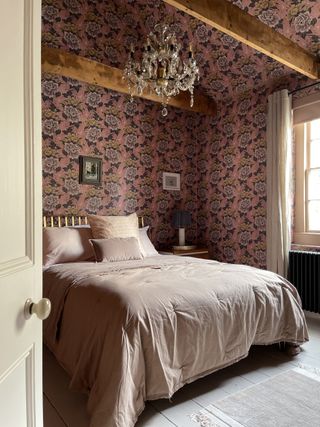 farmhouse style bedroom with beams, chandelier, pink floral wallpaper, white painted wooden floor, blush pink bedding