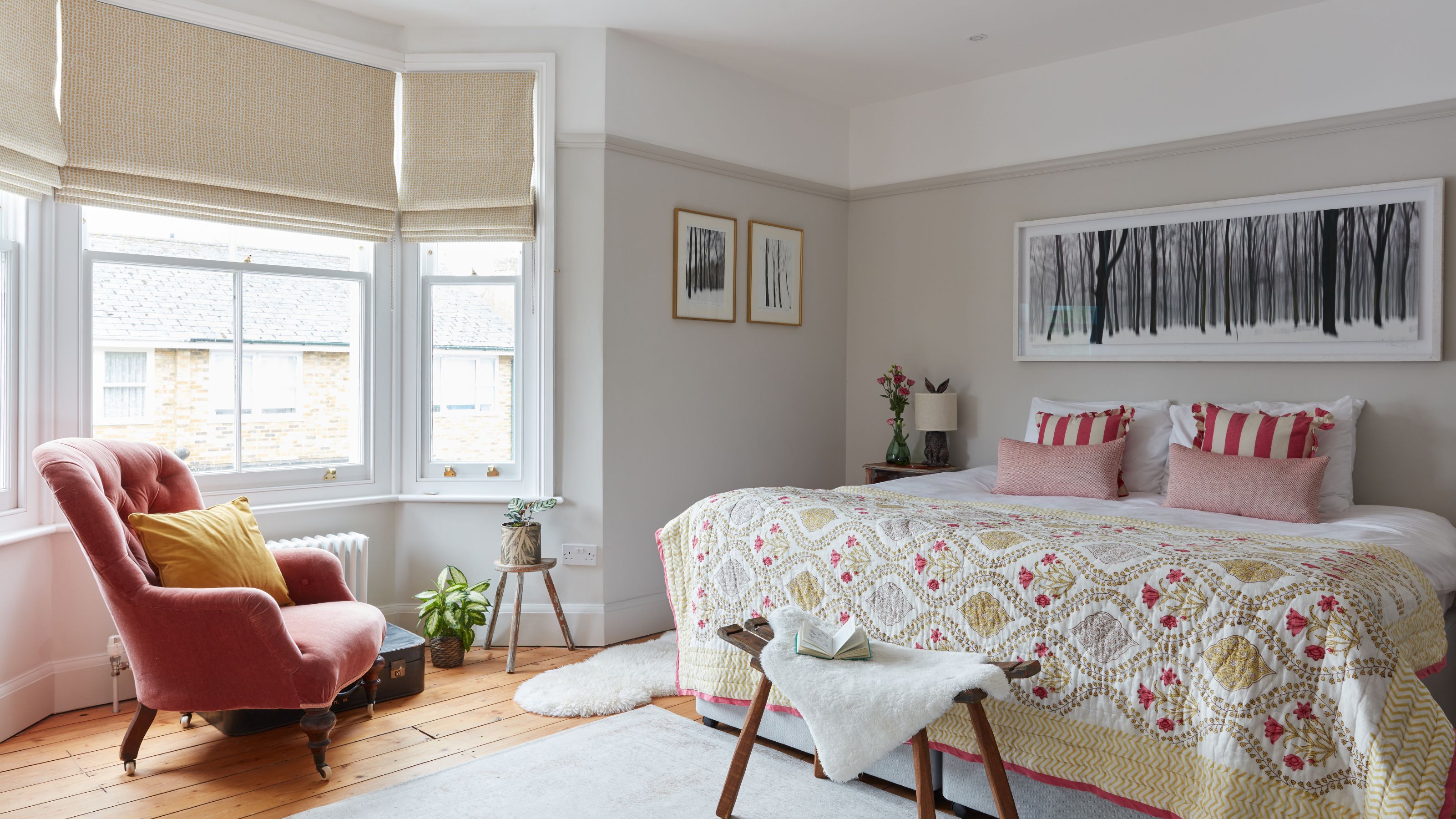Beige painted bedroom with a bay window and an accent chair in front of the large bed