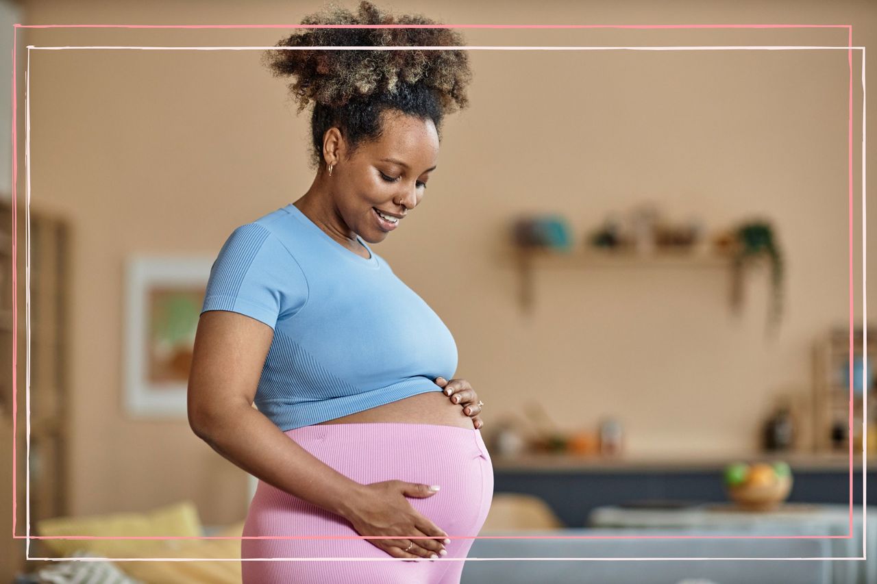 A pregnant woman holds her bump whilst wearing pink and purple sportswear