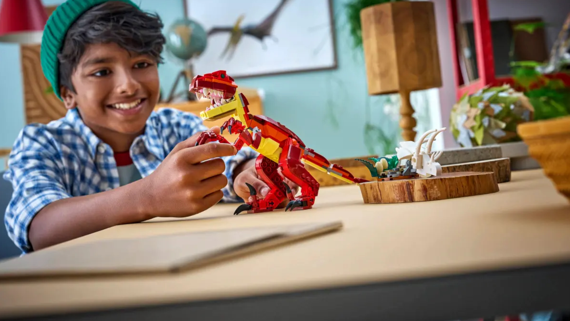 A child smiles while playing with a Lego dinosaur on a wooden table