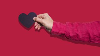 Person's arm holding black paper heart against red background