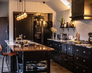 A black kitchen by Melissa Denham with low-hanging pendant lighting, range cooker and kitchen island