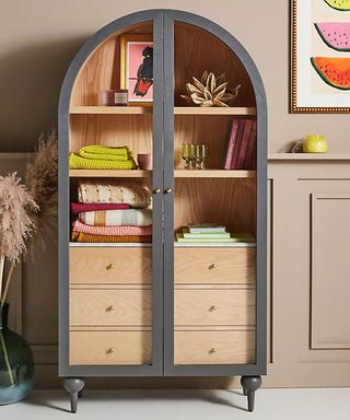glass fronted dresser with arched shape in bare wood and dark grey paint with colourful accessories