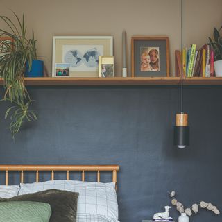 Grey and navy blue wall behind bed seperated by shelf with picture frame, books and plant