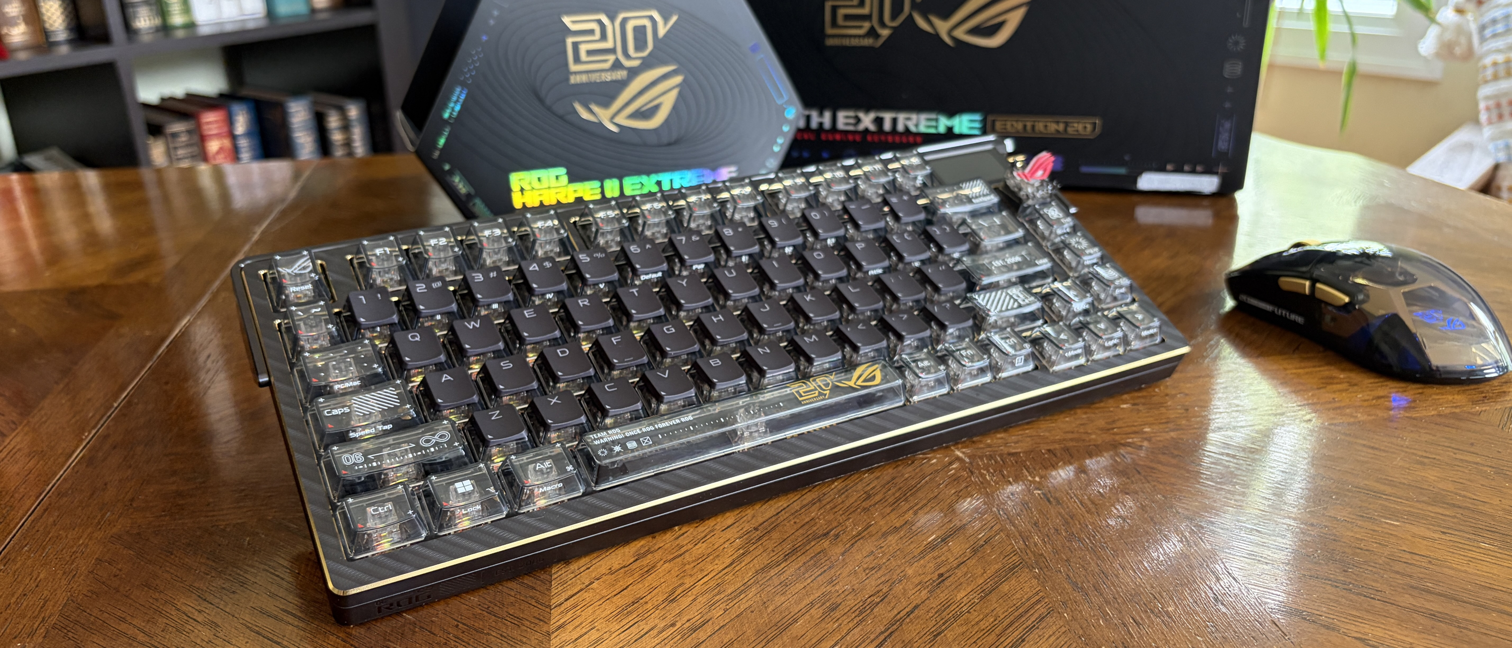ASUS ROG mechanical keyboard and wireless mouse on a wooden table, with ROG-branded boxes in the background.