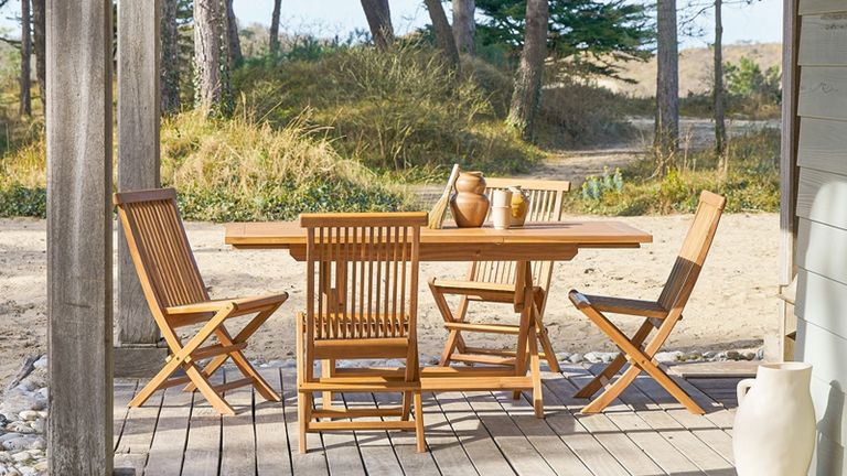 A wooden outdoor table and chair set on a decked patio overlooking the beach