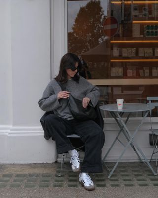 Woman outside coffee shop in grey jumper, black jeans and white trainers