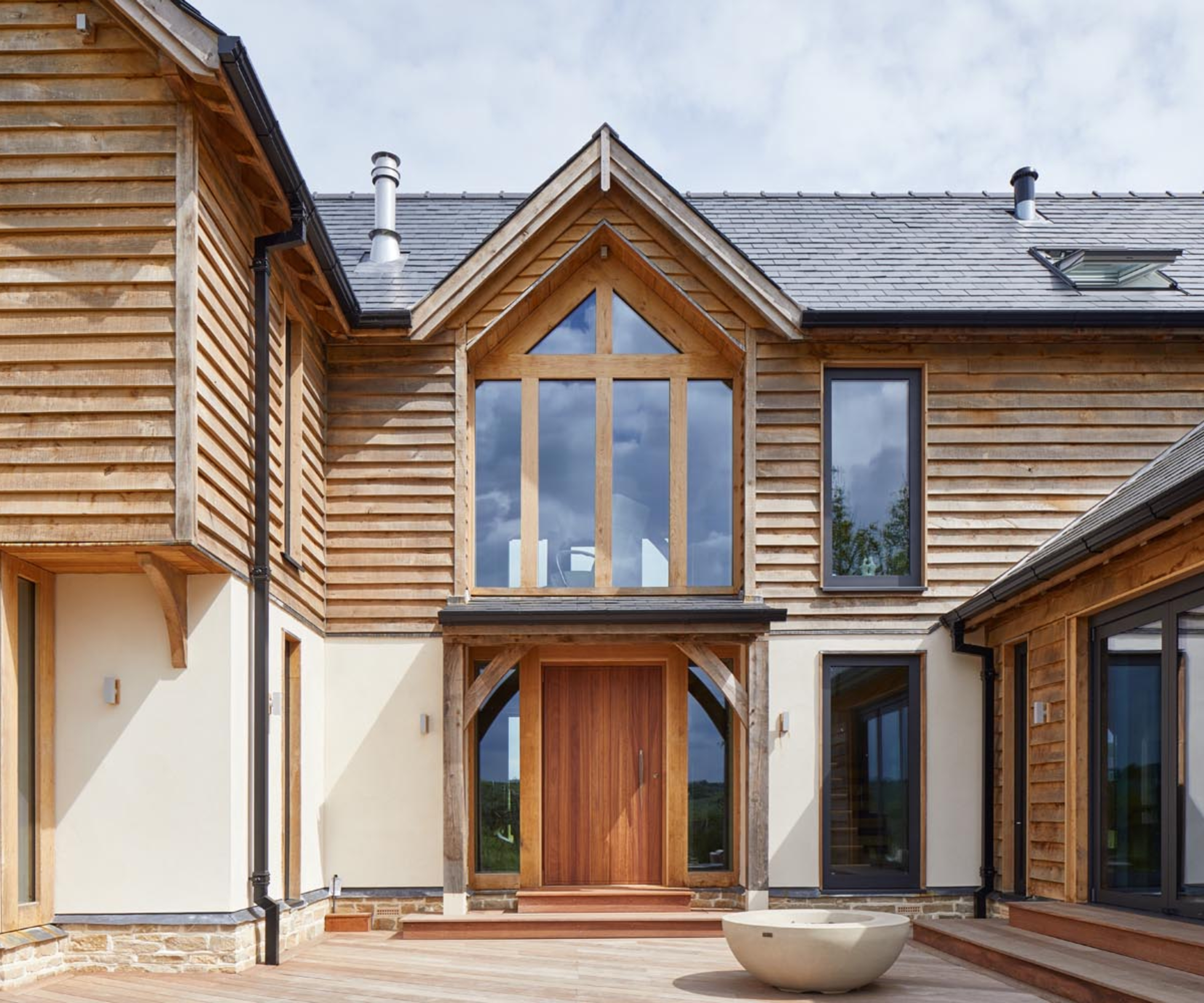 large modern oak framed home with tiled porch canopy support with oak supports, large face glazed window above