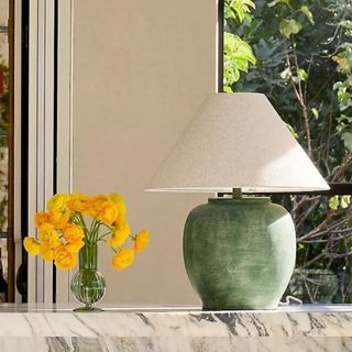 An olive green table lamp next to a vase of flowers