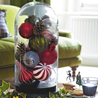 Glass cloche filled with multi coloured baubles, ivy, mince pies and wine on coffee table.