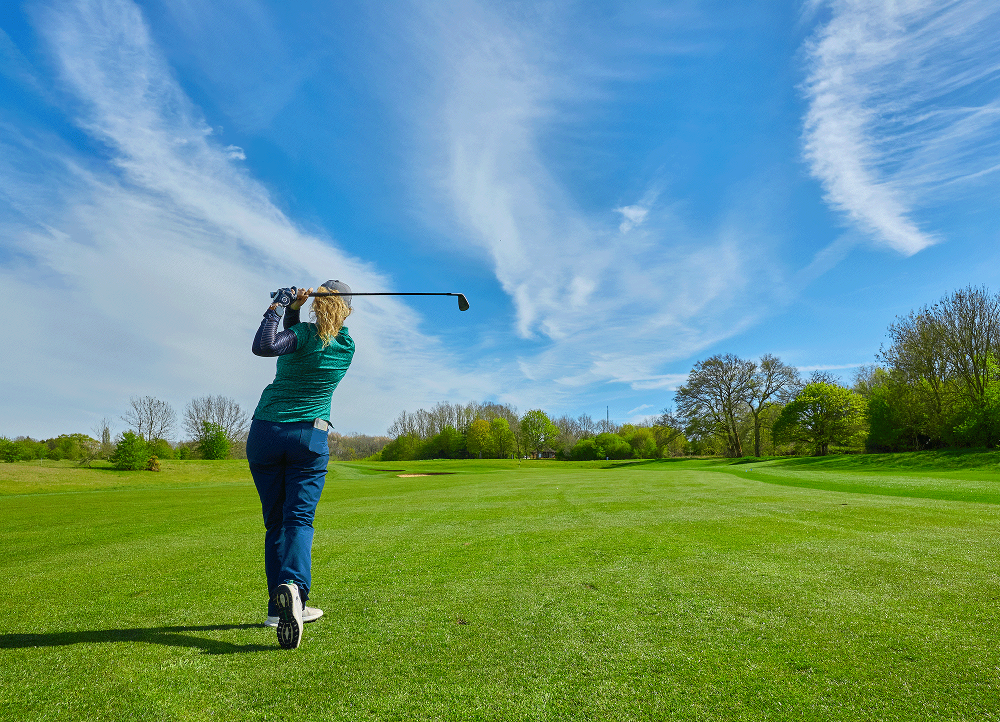 Female amateur golfer in the finish position hitting an iron into a par-5 green