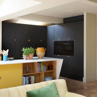 kitchen with black cabinets and yellow and white island, planters and a sofa in the foreground