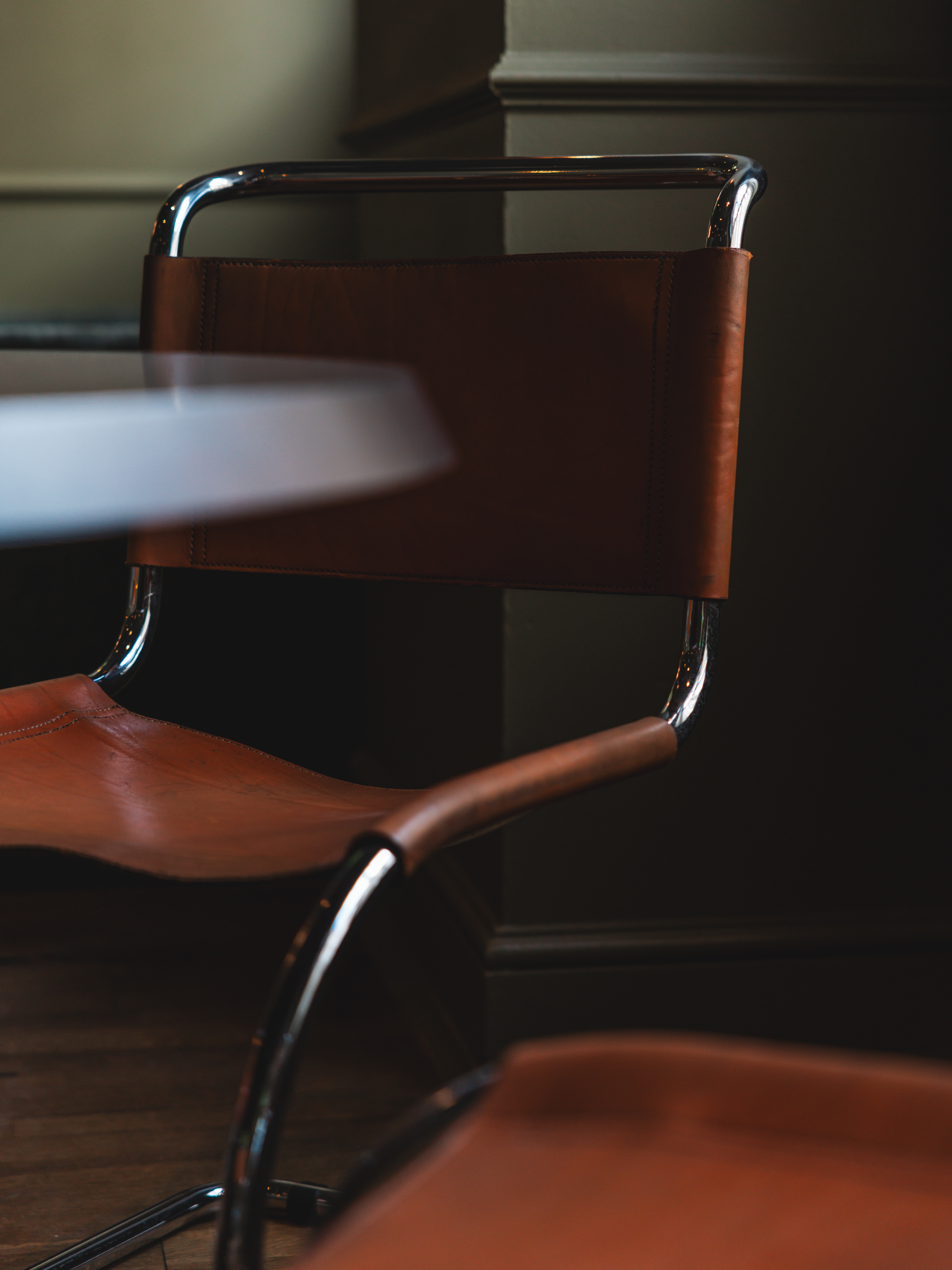 A dark, muted green-tinted hotel lounge with velvety chubby seating in similarly toned nuances, wall art, and wooden furniture.