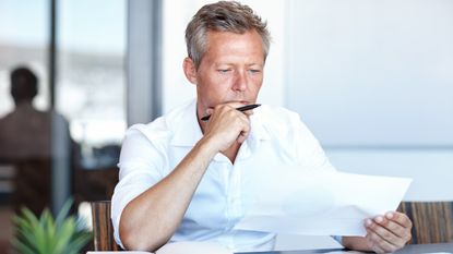 An older man looks over paperwork while sitting at his desk.