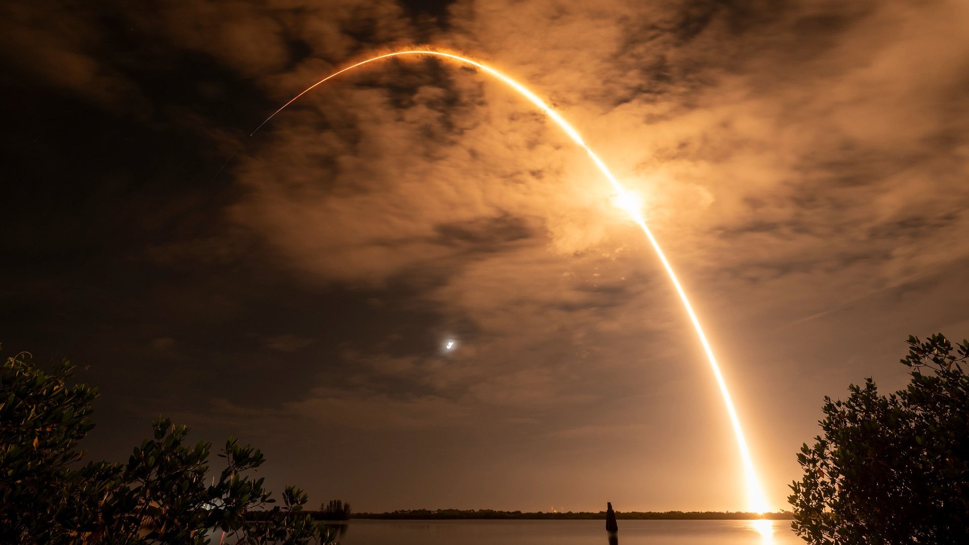 a white rocket launches at night above a streak of fire