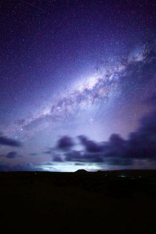 a star studded sky with milky way stretching across the center and some dark clouds below.