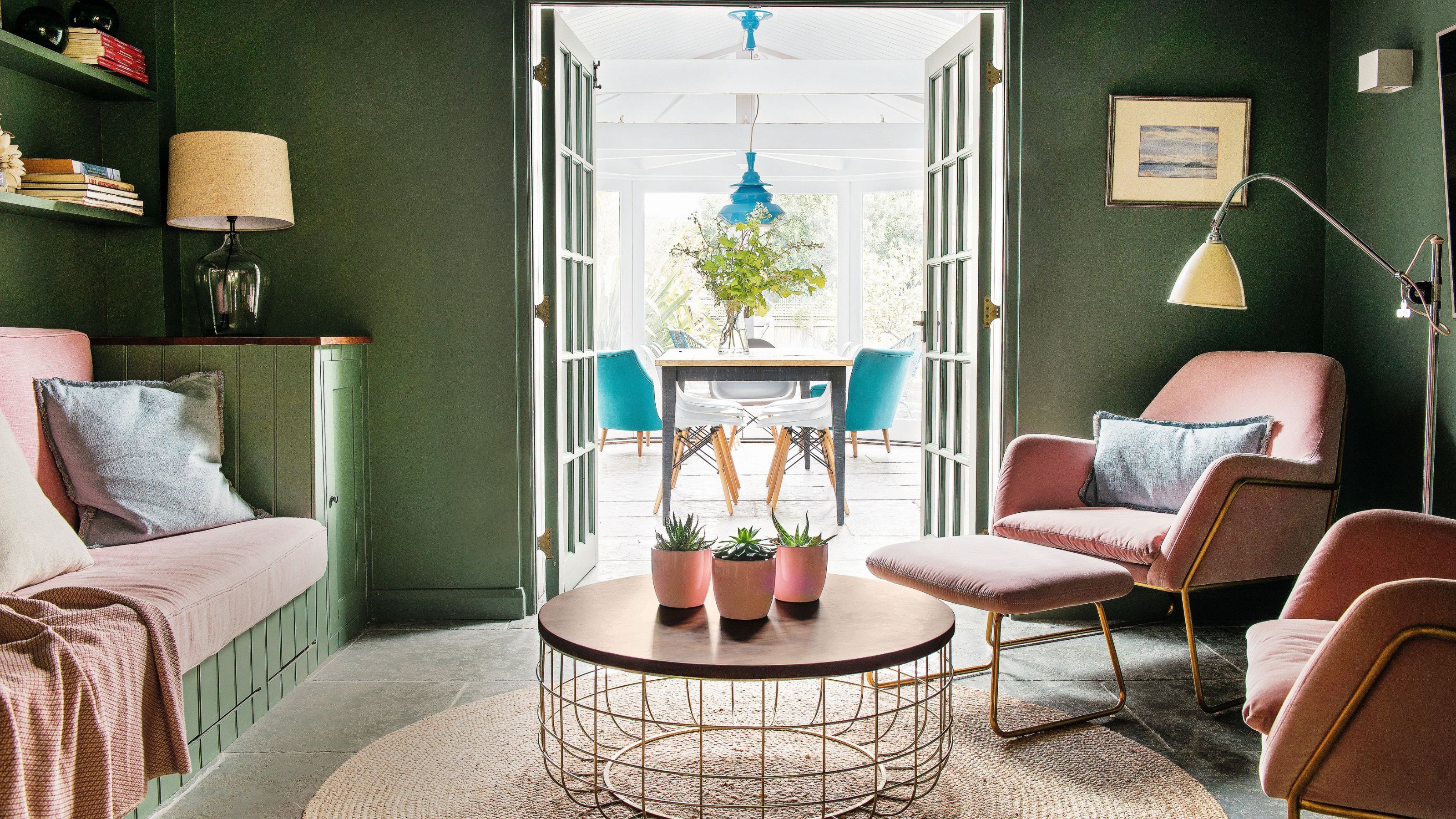 Cosy snug living room with green walls and pink chairs with double doors leading to conservatory