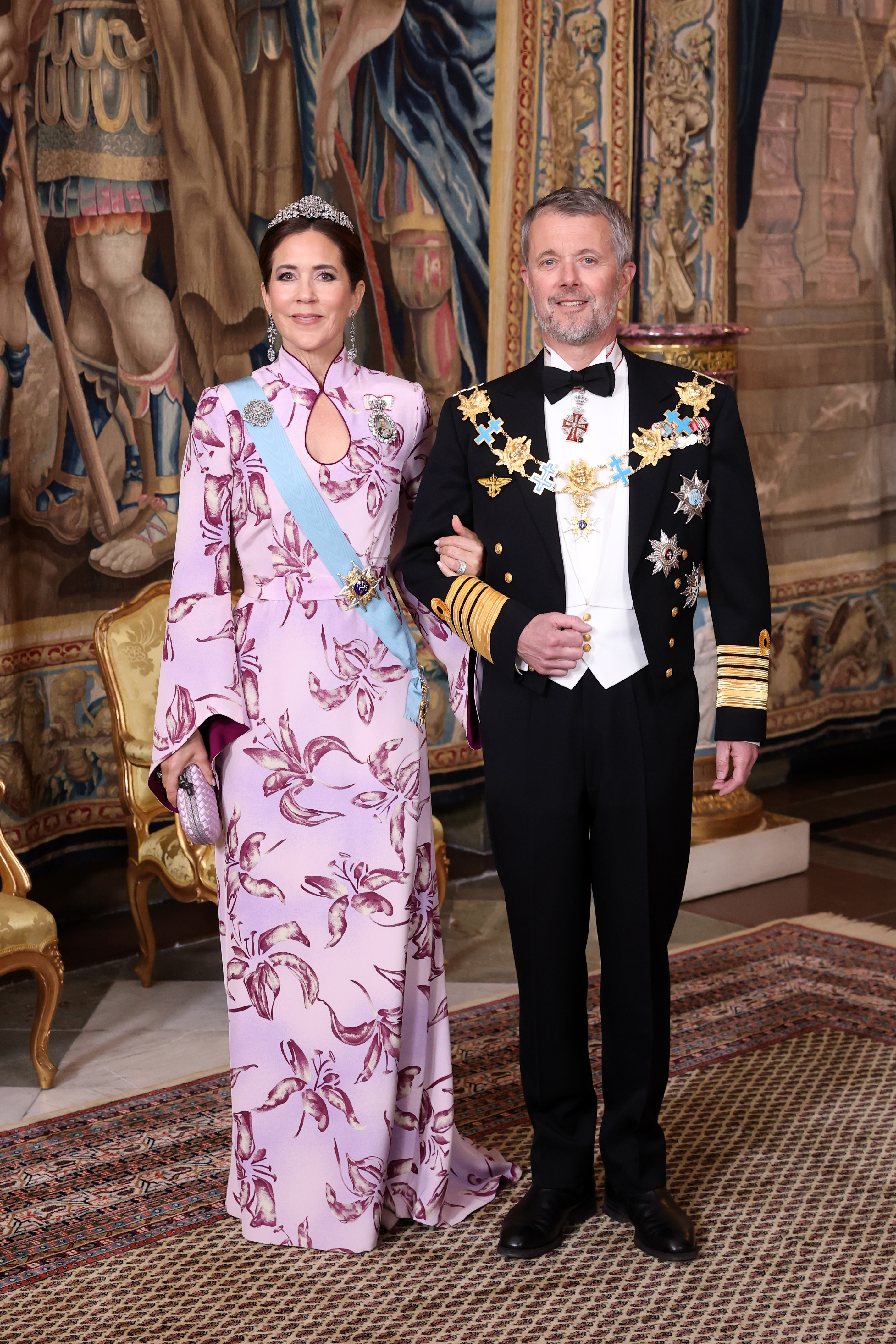 Queen Mary and King Frederik in eveningwear standing in front of a tapestry