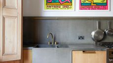 concrete kitchen countertop with bright artwork and timber drawers, brass taps and hanging pots