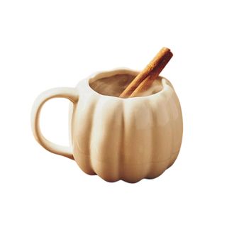 A white pumpkin shaped mug with a cinnamon stick in it