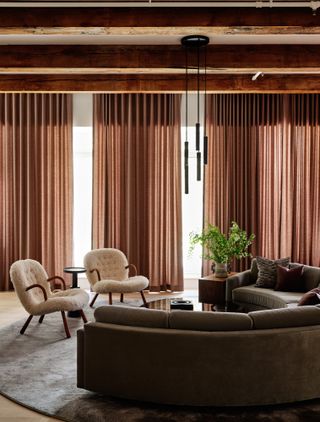 Living room with half-moon curved brown sofa, white boucle armchairs and rust red-brown curtains