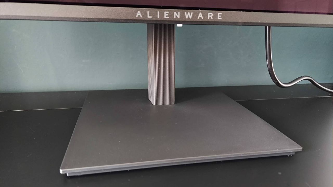 Close up of Alienware AW2726DM base stand on black desk.