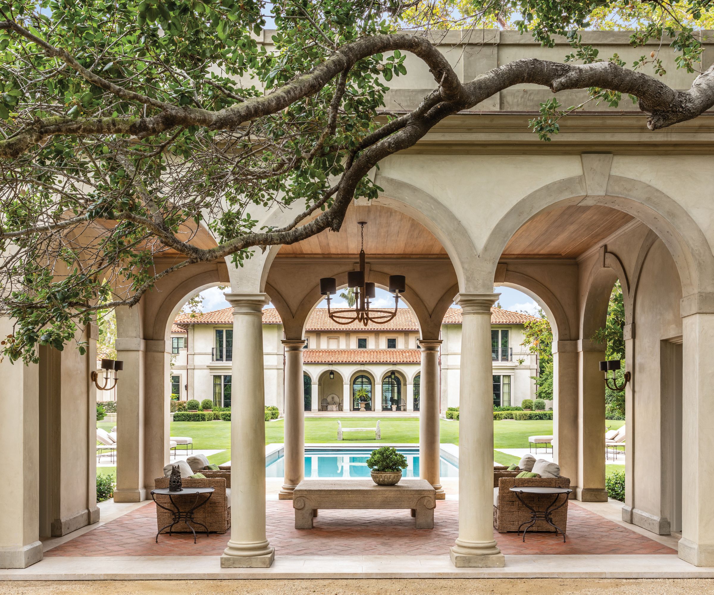 Loggia with arched doorways, terracotta tiled patio, trees and swimming pool
