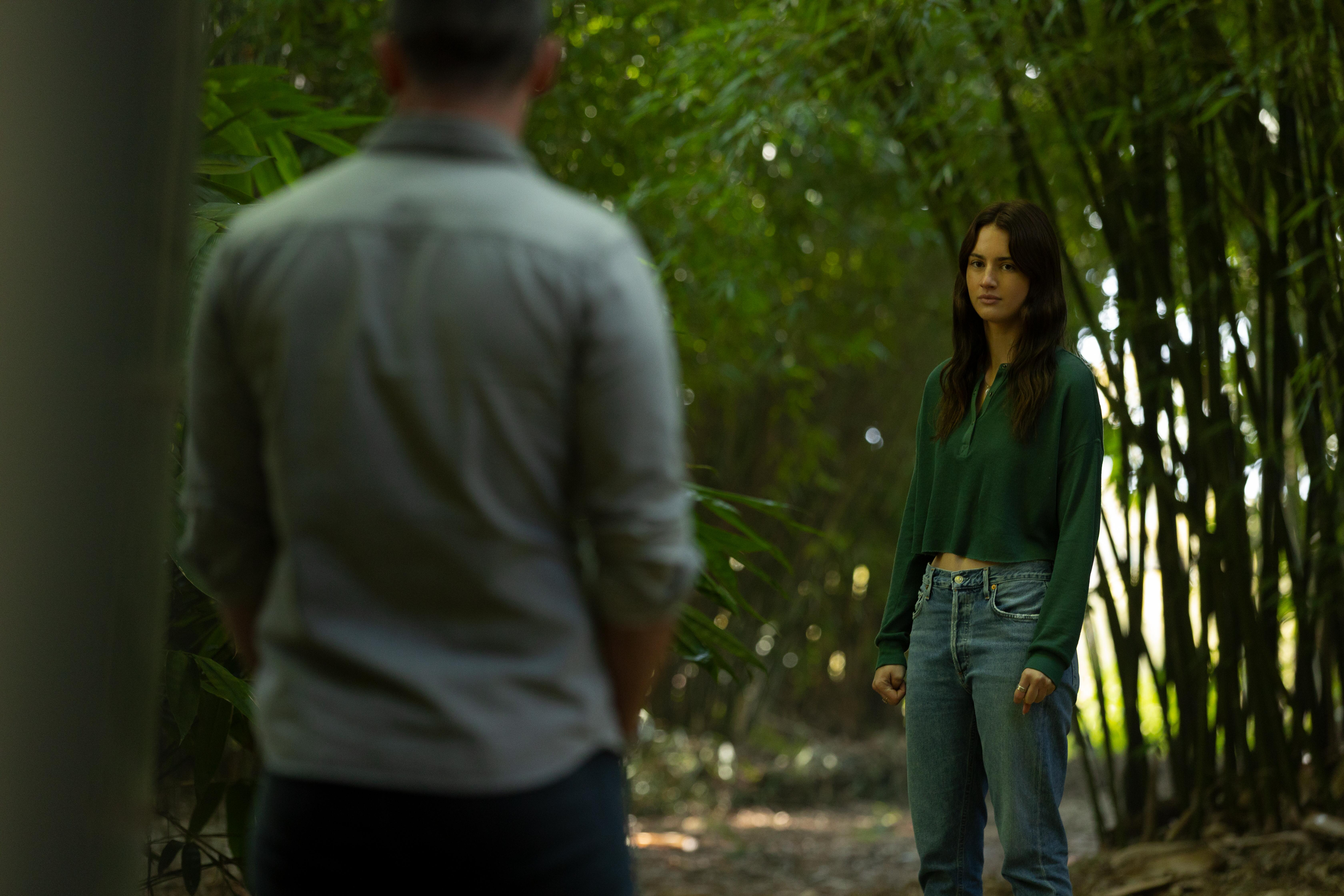 A man with his back to the camera stands with a woman (Grace Van Patten as Zoe) in a forest, in 'Nine Perfect Strangers' season 1.