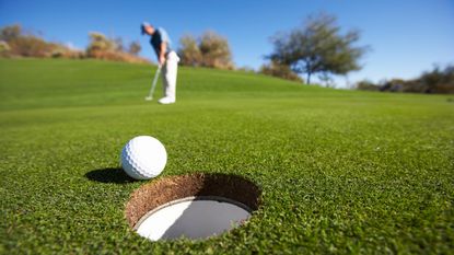 A golfer putts a ball into the hole