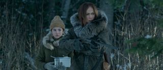 Jennifer Lopez aims her shotgun while Lucy Paez stands behind her in the snowy woods in The Mother.