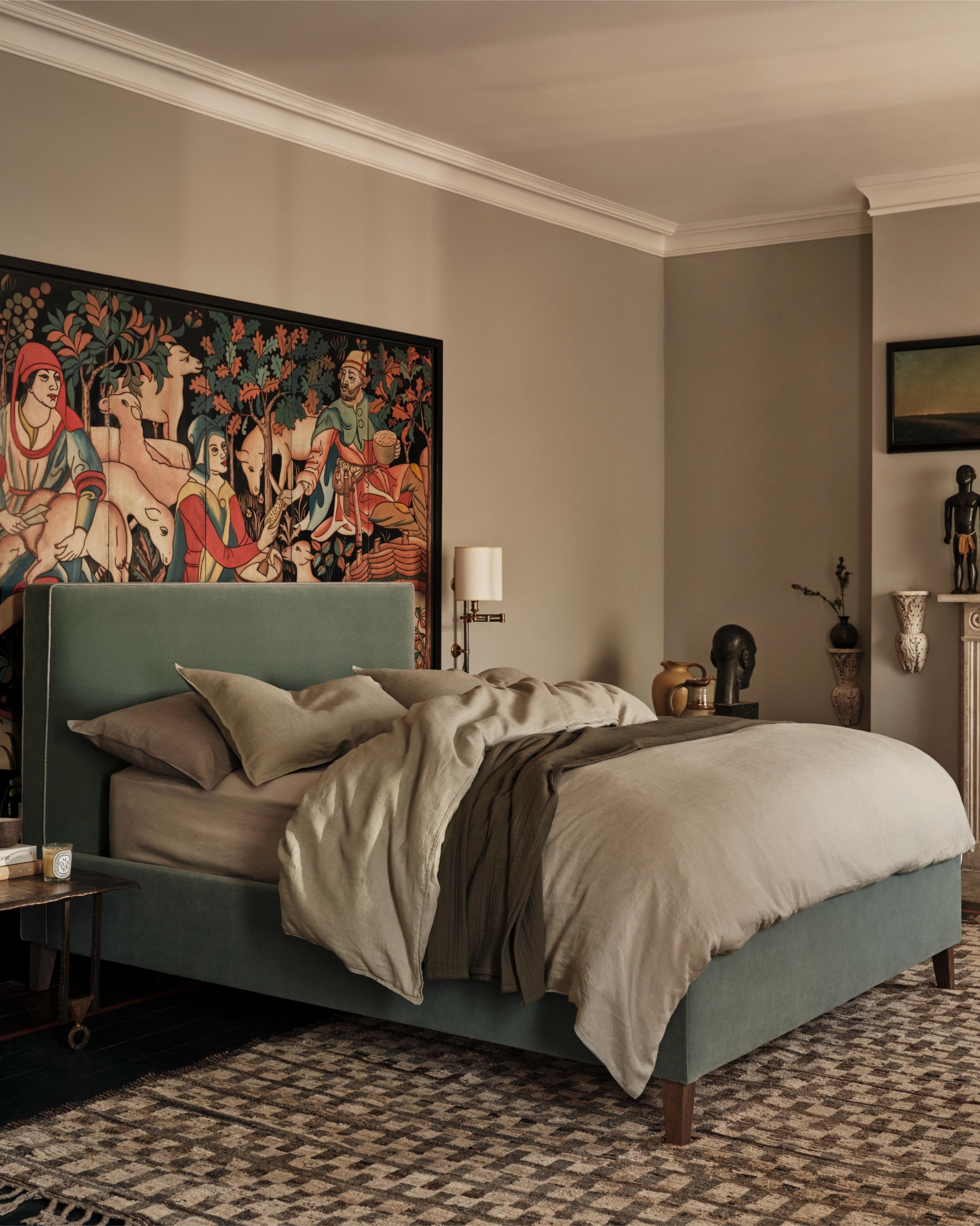 Image of a navy upholstered bed with beige bedding in a boho-style room. There is a patterned rug on the floor and mural panelling behind the bed.