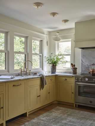 yellow kitchen with marble counter, floor rug, freestanding silver stove, cream walls, white ceiling with statement lighting, brass taps and timber floors