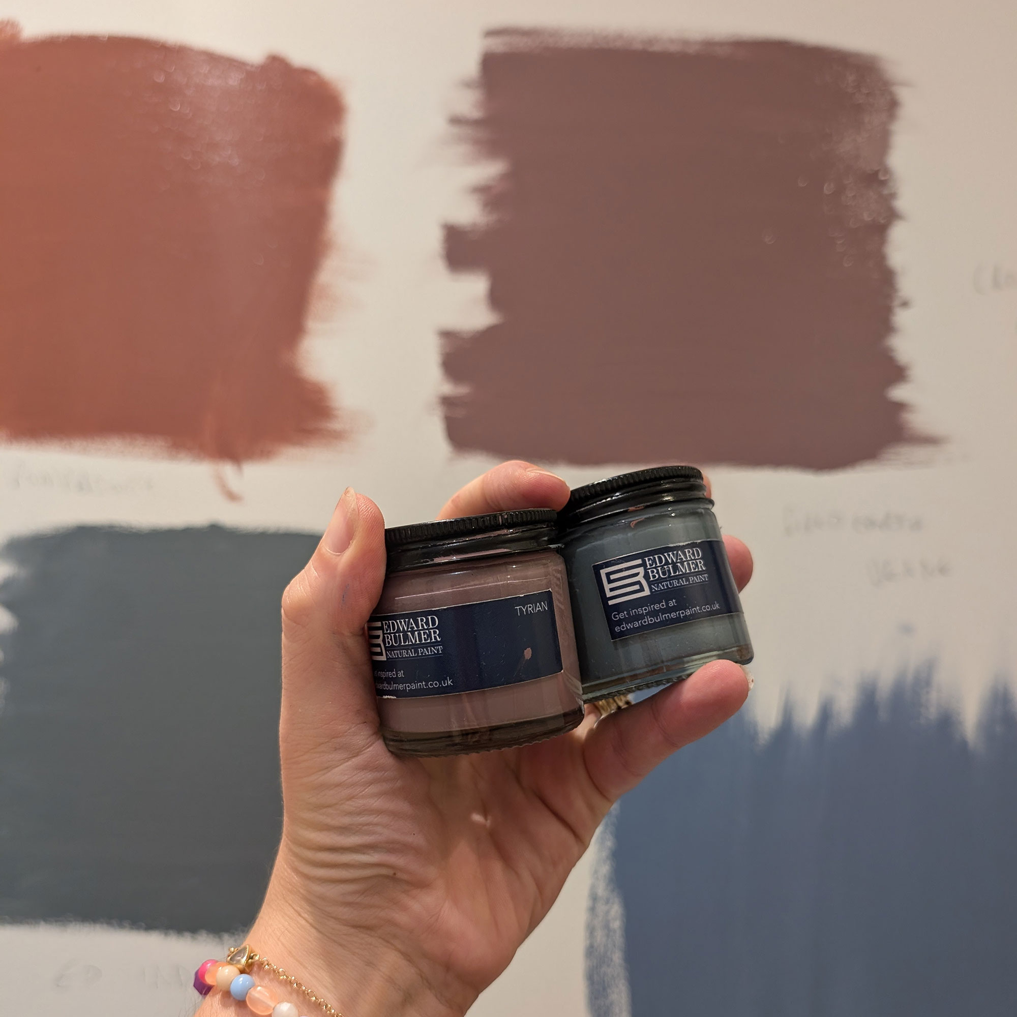Person holding up sample paint pots in front of wall with swatches
