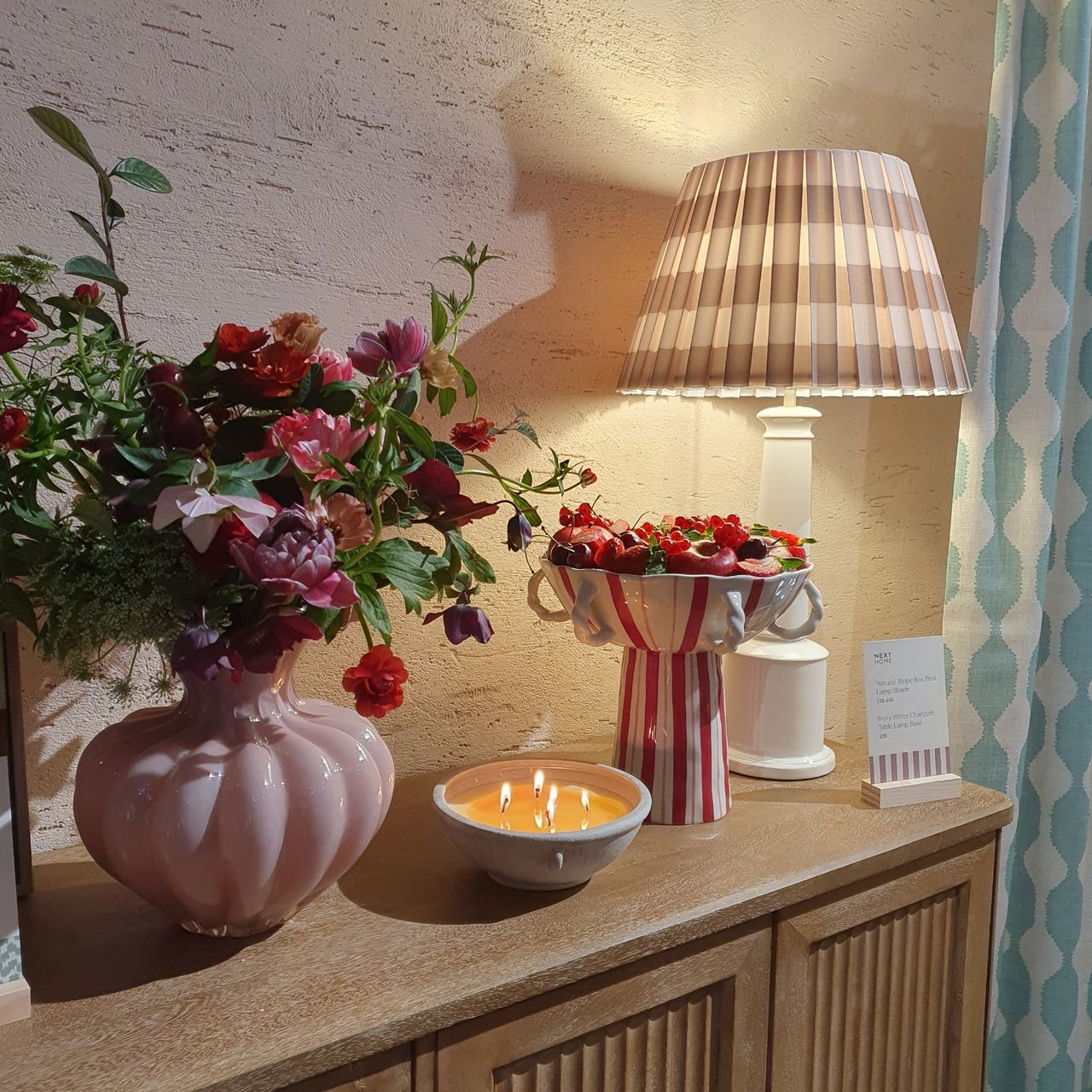 A sideboard styled with Next's pink vase, striped stand bowl and a table lamp with a pleated striped shade at the launch event for the Decorator range