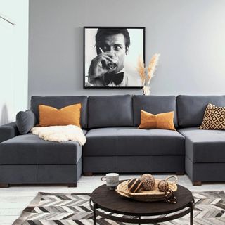 A grey modular sofa bed with orange cushions and a black and white picture of a man's face hung on the wall behind