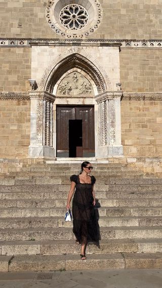 Woman wearing sheer black dress while standing on the step of an Italian church.