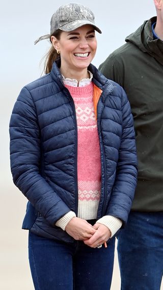 Kate Middleton stands wearing a puffer jacket, Fair Isle jumper and baseball cap on West Sands beach in 2021