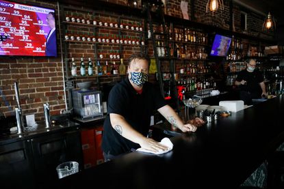 A bartender wearing a face mask wipes down the bar.