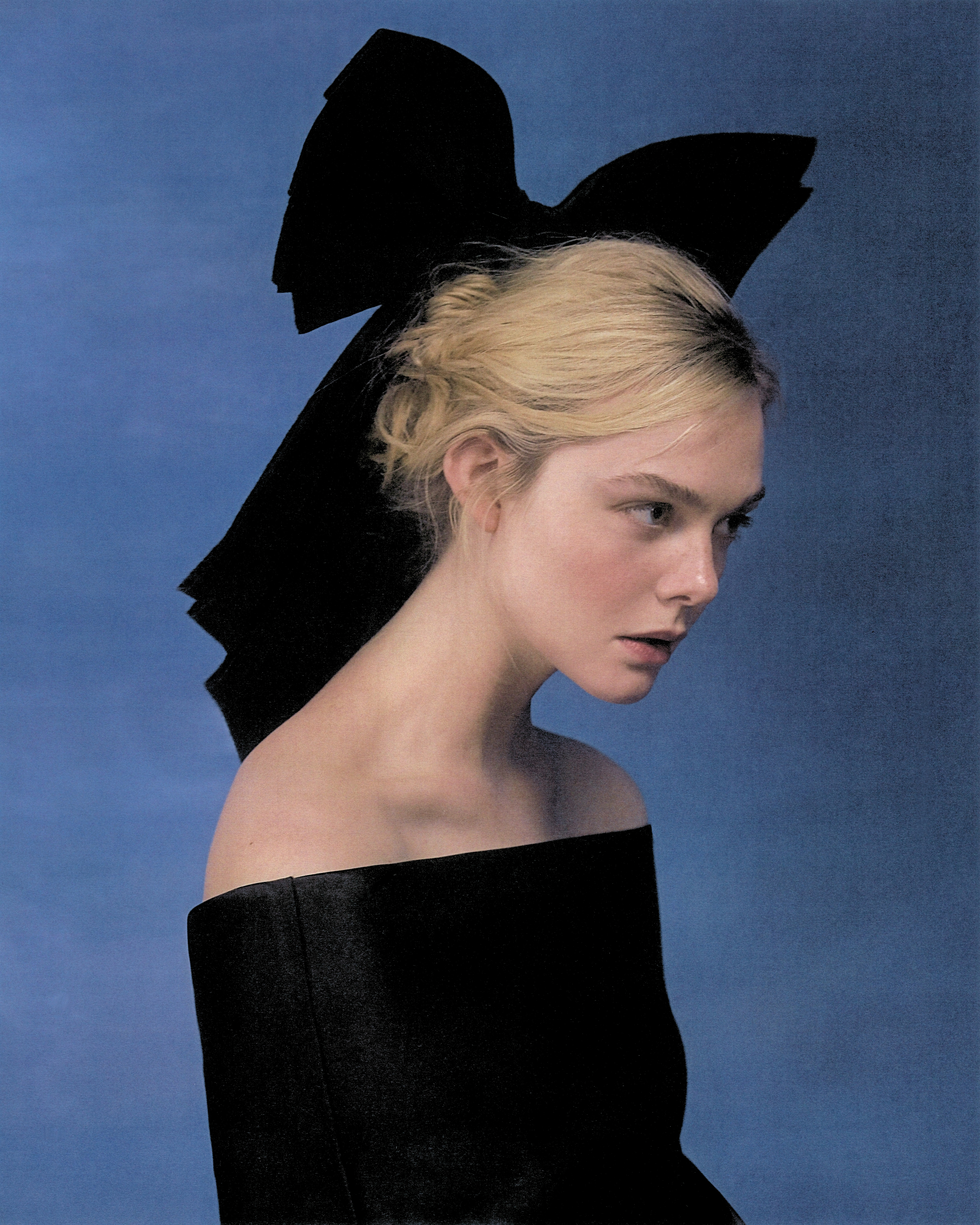 Elle Fanning shot by Szilveszter Mak&amp;oacute;. She is looking off camera wearing an off-the-shoulder black top and an oversize black bow.