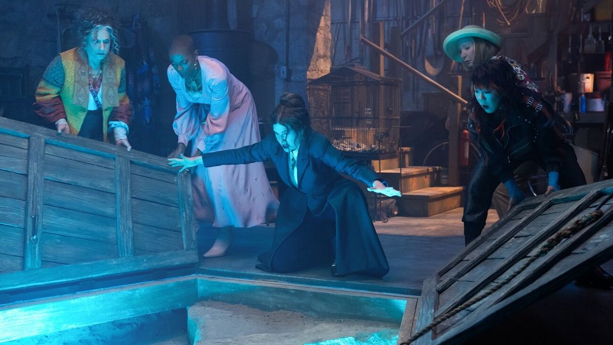 A blue light bathes Agatha Harkness (Kathryn Hahn) and her new coven as they peer into a cellar in new Disney Plus series Agatha All Along