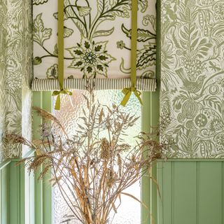 decorative green and white swedish blinds over a small window flanked by wallpaper and green panelled walls .jpg