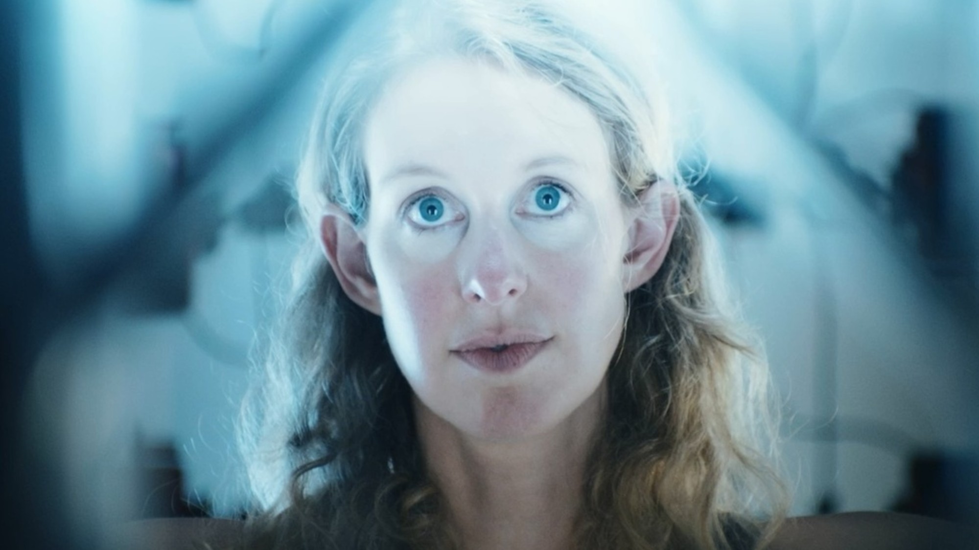 A close up of Elizabeth Holmes with a light flare coming in from the top and everything around her out of focus. 