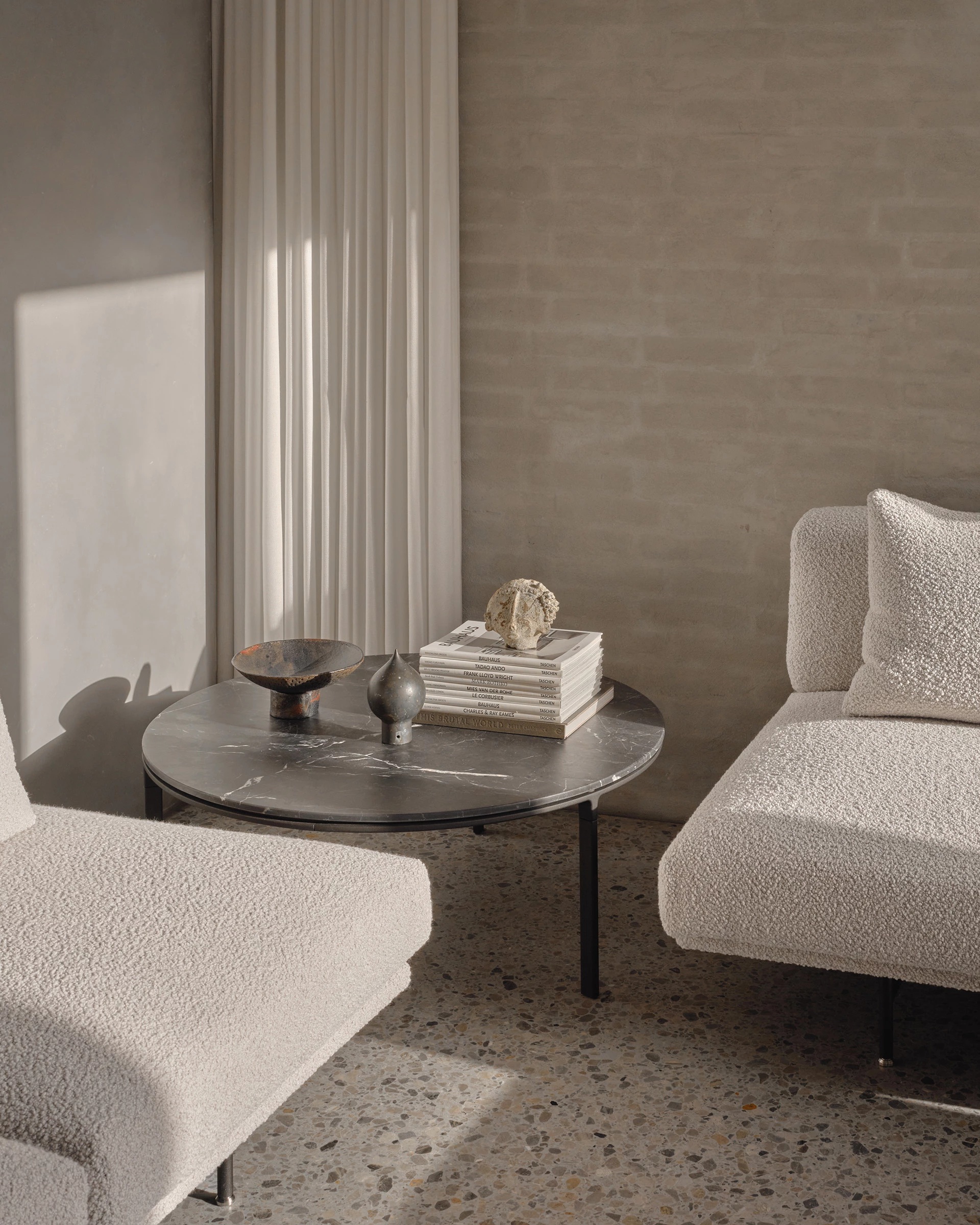 A neutrally decorated Danish apartment houses a series of sculptural furnishings in white or grey hues, terrazzo flooring in similar tones, and printed matter collectibles sitting on a coffee table and topped with paperweights.